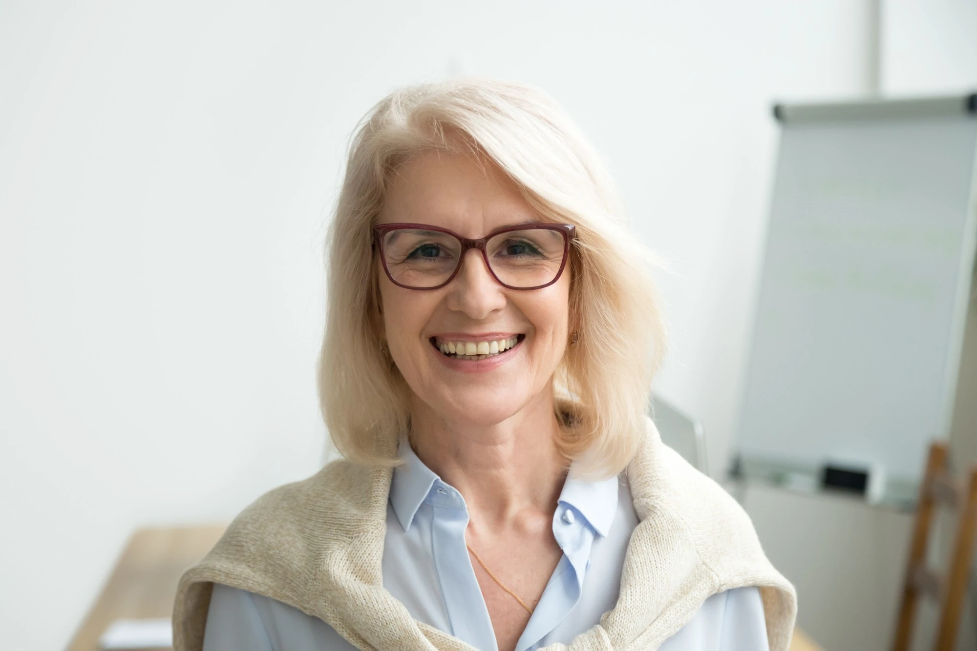 A Woman Wearing Glasses And A Scarf Smiles Warmly At The Camera.